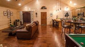 A cozy wooden cabin interior with a dining area, a pool table, and a living room with a sofa and coffee table. - As You Wish Cabin in a breathtaking one-bedroom honeymoon cabin that is the perfect place to make lasting memories with each other. (Broke Bow)