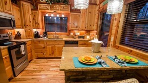 Una cocina con armarios de madera, una isla de piedra y un comedor con una silla tejida.