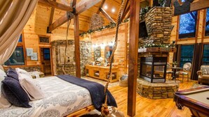 Un acogedor interior de cabaña de troncos con una cama, chimenea de piedra y una mesa de billar.