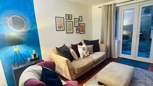 Una sala moderna con un sofá, un sillón y un reposapiés, un espejo grande y una pared con cuadros enmarcados.