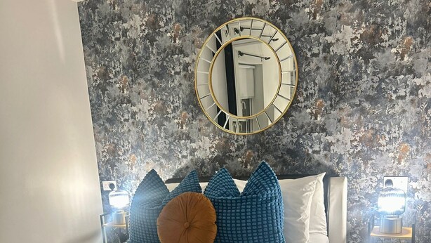 Un dormitorio con cama, espejo redondo y pared con textura.