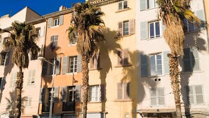 Un edifici de diverses plantes amb balcons, palmeres i una botiga amb un rètol.