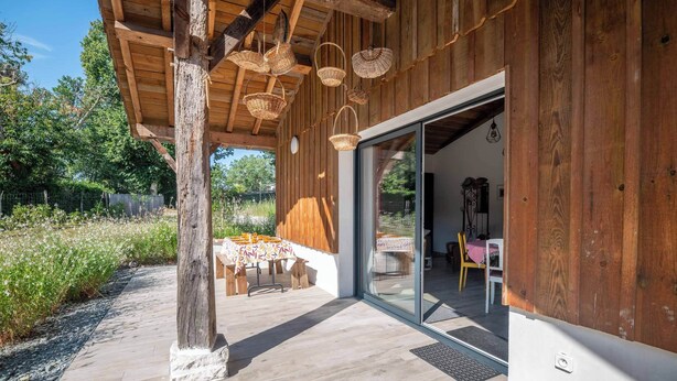 A wooden building with a covered patio, outdoor seating, and a glass door leading inside.