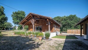 A wooden cabin with a sloped roof, a front porch, and a small garden area with potted plants and a lawn.