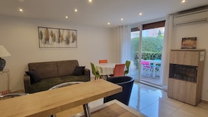 A living room with a sofa, a dining table, and a glass door leading to an outdoor area with a table and chairs.