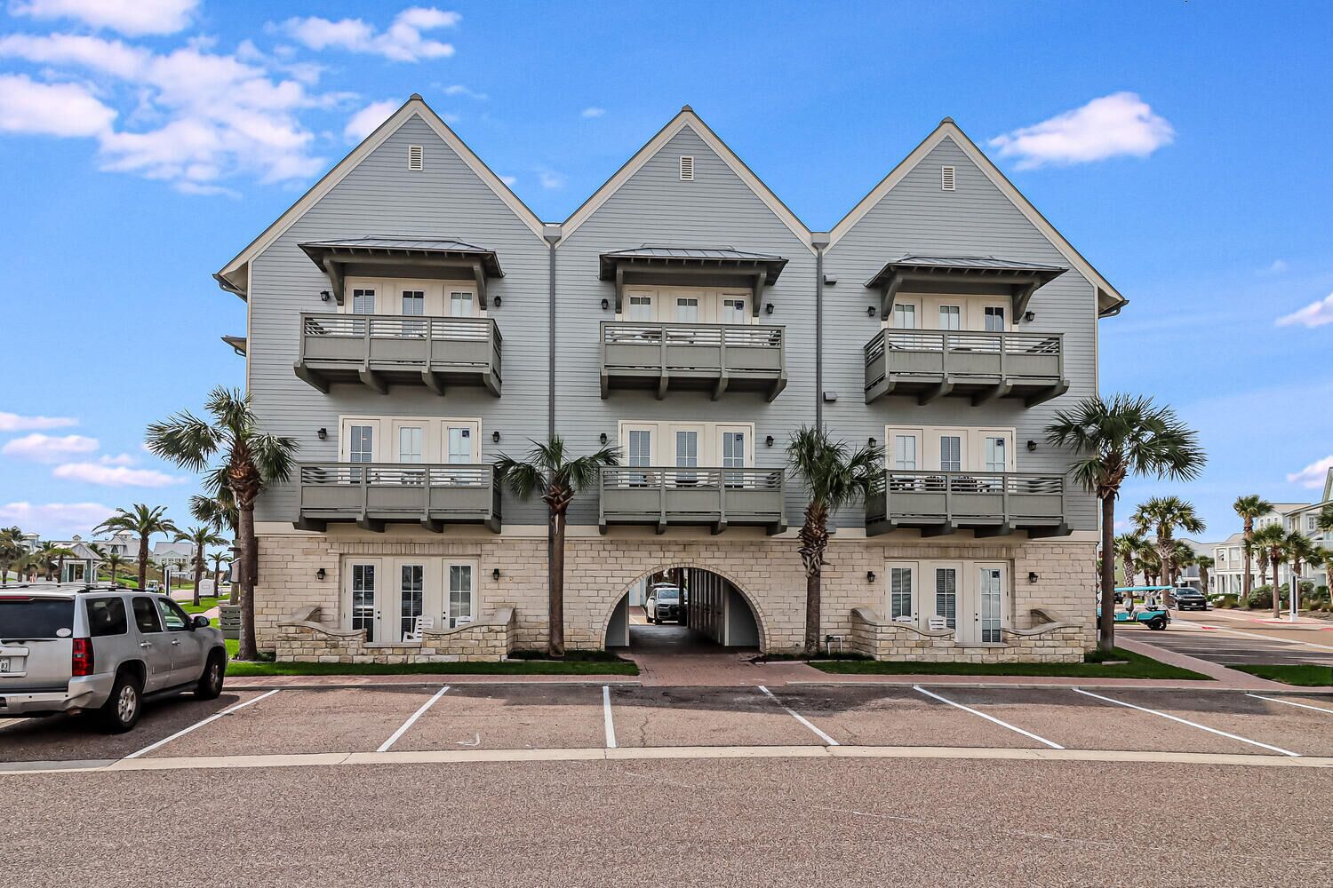 A three-story building with balconies, a central entrance, and a parking lot.