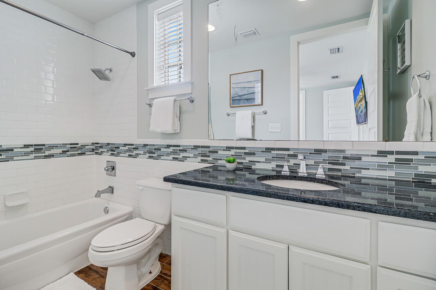 Een moderne badkamer met een wit toilet, een badkuip en een wastafel met een backsplash van mozaïektegels.
