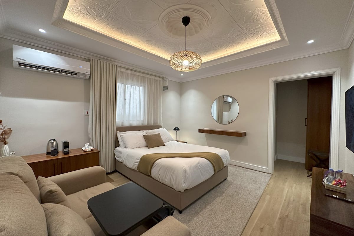 A modern bedroom with a large bed, a sofa, a small table, and a ceiling light fixture.