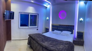 A modern bedroom with a bed, a window, and a wall-mounted TV. - BEST HOME STAY IN VRINDAVAN (Vrindavan)