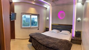 A modern bedroom with a bed, a window, and a TV mounted on the wall. - BEST HOME STAY IN VRINDAVAN (Vrindavan)