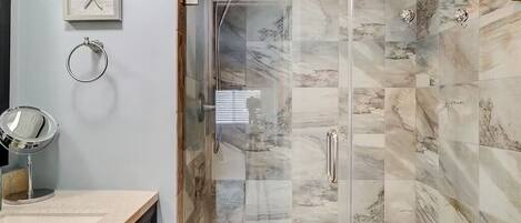 A bathroom with a glass-enclosed shower, marble tiles, a vanity with a mirror, and a framed starfish decoration.