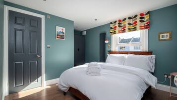 A bedroom with a bed, a window with a view, a door, and a wall-mounted light fixture.