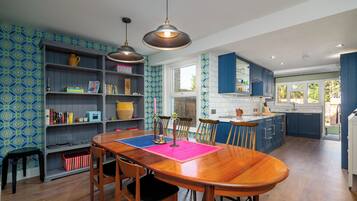 A modern kitchen with a wooden dining table, blue cabinets, and patterned wallpaper.