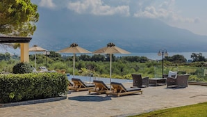 Ein Poolbereich mit Liegestühlen und Sonnenschirmen, mit Blick auf eine malerische Landschaft mit Bergen und einem See.