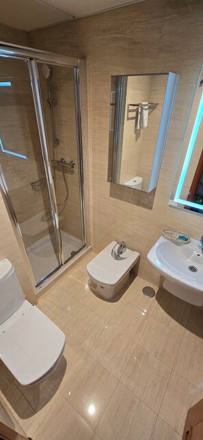 Une salle de bain moderne avec une douche à parois de verre, des toilettes blanches et un lavabo surmonté d’un miroir.