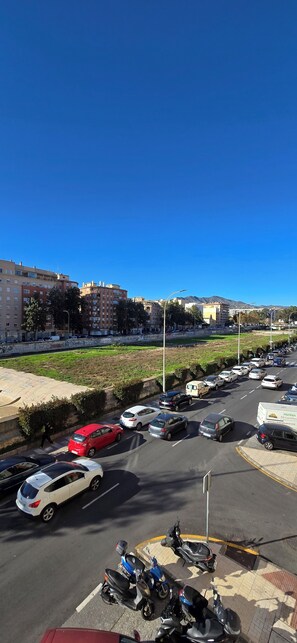 Un parking rempli de voitures et de scooters, entouré de bâtiments et surplombé par un ciel bleu dégagé.