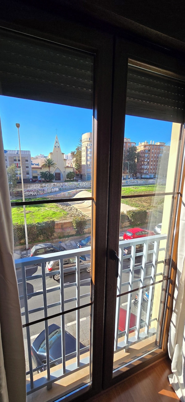 Une vue depuis une fenêtre avec des barreaux en métal, une église et un parking rempli de voitures.
