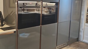Una cocina moderna con horno y microondas integrados, suelo de madera, y un perro en primer plano.