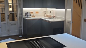 Una cocina moderna con encimera blanca, estufa integrada y un lavabo. Se observa una ventana con vistas al exterior.