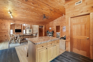 A wooden cabin interior with a kitchen area featuring a granite countertop, wooden cabinets, and a ceiling fan. - Ridgeview Retreat | Hocking Hills, Hot Tub, Sauna (South Bloomingville)