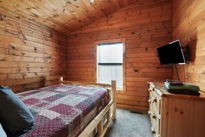 Una habitación de cabaña de madera con una cama, un aparador y un televisor montado en la pared.