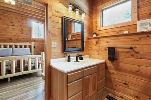 A wooden cabin interior with a bed, a sink, and a mirror. - Ridgeview Retreat | Hocking Hills, Hot Tub, Sauna (South Bloomingville)
