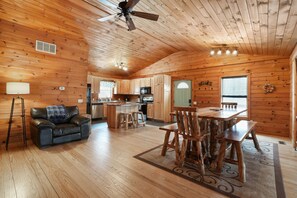 A cabin interior with a wooden interior, a dining area, a kitchen, and a living room with a sofa and a lamp.