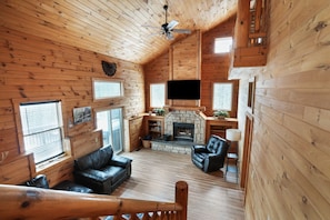 Interior de una cabaña de troncos con chimenea, sofás de cuero y un televisor de pantalla plana.