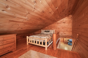 Une chambre dans une cabane en bois, avec un lit, une commode et une petite table.