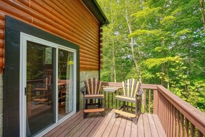 A wooden deck with two Adirondack chairs and a table, overlooking a forested area. - Ridgeview Retreat | Hocking Hills, Hot Tub, Sauna (South Bloomingville)