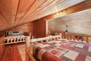 A cozy wooden cabin bedroom with a bed, a chair, a desk, and a window with blinds. - Ridgeview Retreat | Hocking Hills, Hot Tub, Sauna (South Bloomingville)