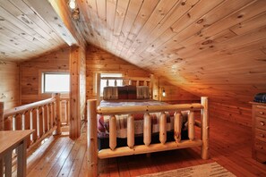 A wooden cabin bedroom with a bed, a window, a dresser, and a wooden railing. - Ridgeview Retreat | Hocking Hills, Hot Tub, Sauna (South Bloomingville)