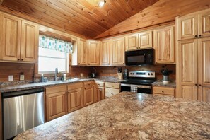 A kitchen with wooden cabinets, granite countertops, a stainless steel dishwasher, a microwave, and an oven. - Ridgeview Retreat | Hocking Hills, Hot Tub, Sauna (South Bloomingville)