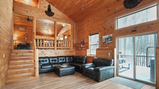 A log cabin interior with a leather sofa, wooden floors, and a large sliding glass door to the outside.