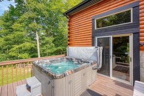 Una cabaña de madera con un jacuzzi en una terraza, rodeada de árboles.