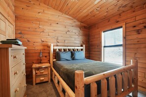 A wooden cabin bedroom with a bed, dresser, and window. - Ridgeview Retreat | Hocking Hills, Hot Tub, Sauna (South Bloomingville)