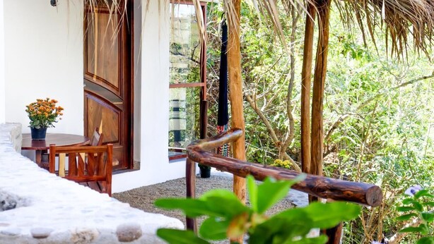 Un área de estar al aire libre con encanto, con mesa y sillas de madera, techo de paja y vistas a exuberante vegetación.