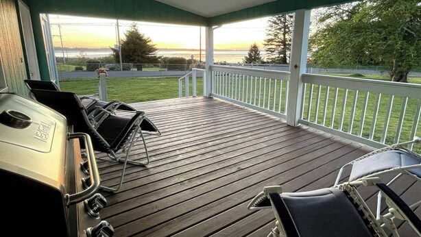 A covered outdoor deck with a grill and lounge chairs, overlooking a grassy area and a body of water. - Rosie's Surf Shack: 3 BR, 2 BA house in beautiful Grays Harbor (Grays Harbor County)