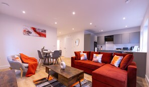 Relax in this stylish living area with a sofa, armchair, and dining table, surrounded by modern appliances and a beautiful abstract art piece.