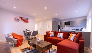 Relax in this stylish living area with a sofa, armchair, and dining table, surrounded by modern appliances and a beautiful abstract art piece.