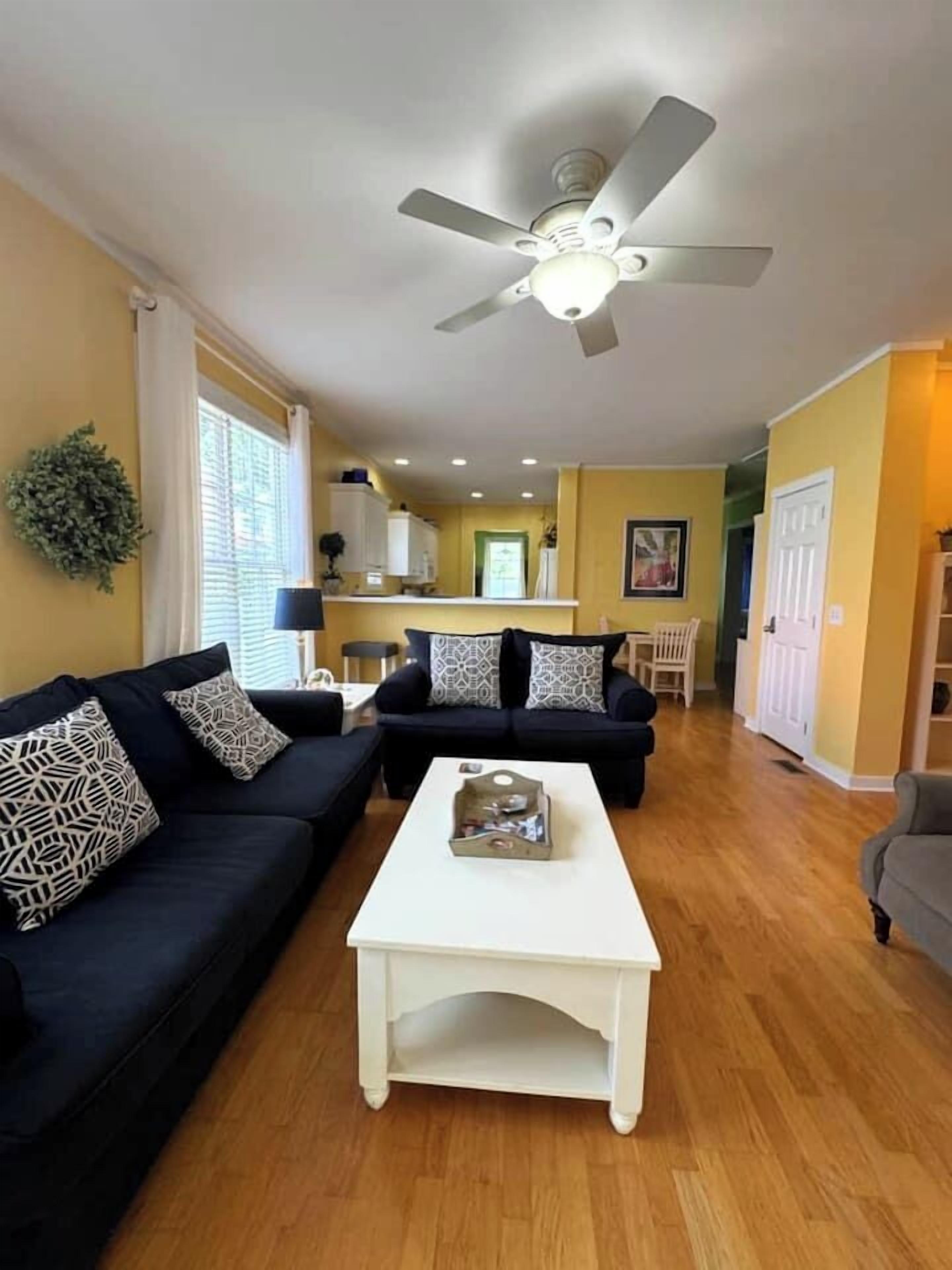Ein Wohnzimmer mit einem dunkelgrauen Sofa, einem weißen Couchtisch und einem Deckenventilator.