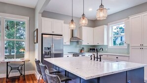 Een moderne keuken met een ruim kookeiland, witte keukenkastjes en hanglampen.