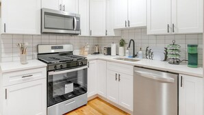A modern kitchen with white cabinetry, stainless steel appliances, and a wooden floor. - City Center Oasis Newark (Newark)