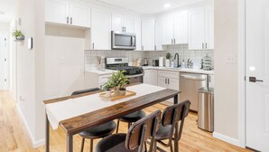 A modern kitchen with white cabinets, a stainless steel stove, and a dining area with a wooden table and four chairs. - City Center Oasis Newark (Newark)