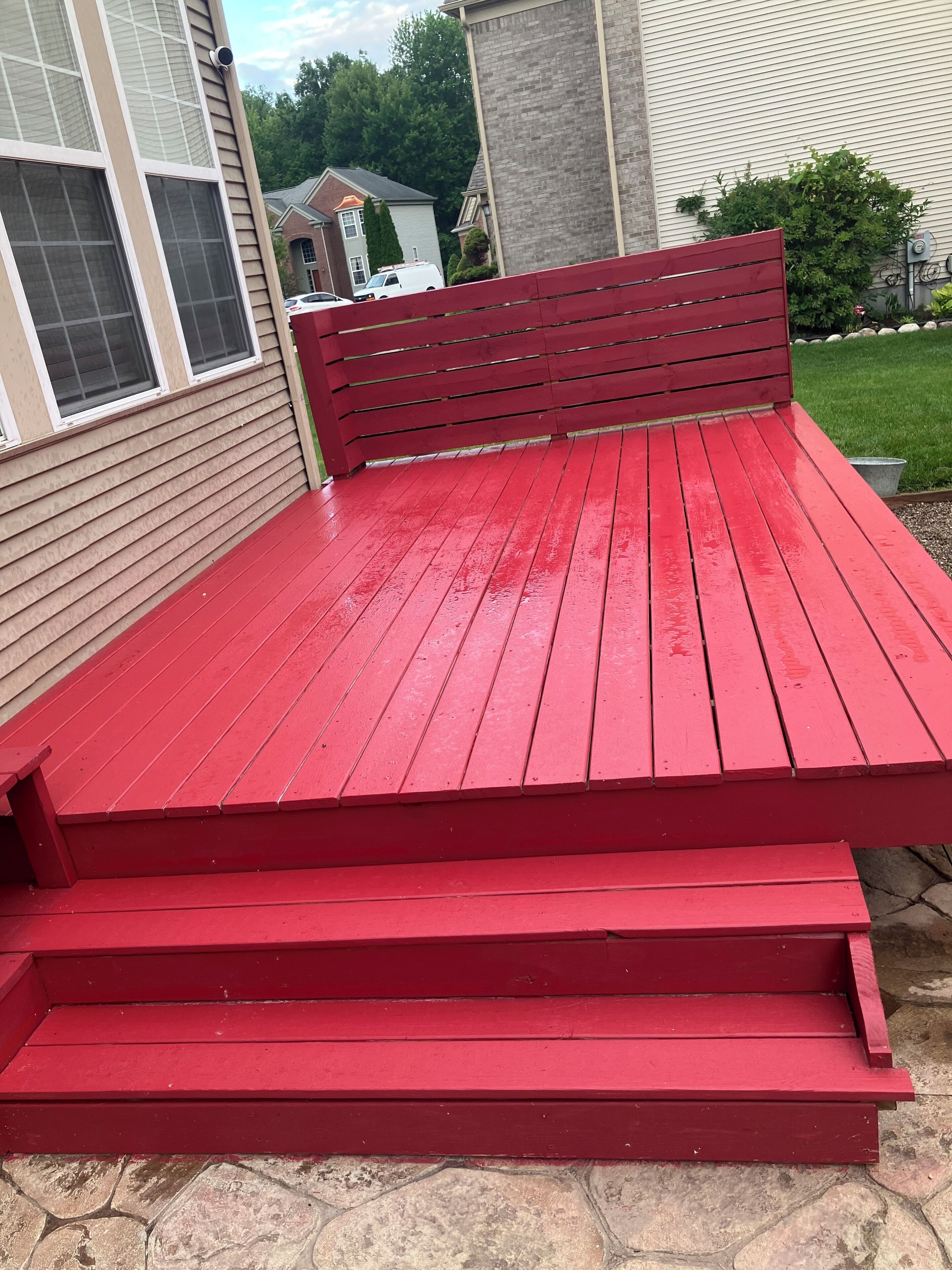 A red wooden bench with steps leading up to it, positioned against a house with beige siding and a brick chimney.