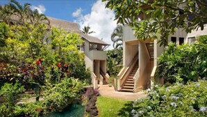 Ein tropischer Garten mit einem Pool, einer Holztreppe und einem Gebäude mit Ziegeldach.