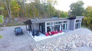 Ett modernt hus med en täckt uteplats, en grusuppfart och en rad röda stolar.