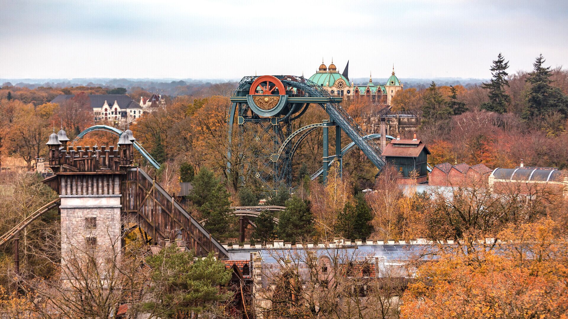 A roller coaster with a large wheel, a castle-like structure, and a building with domes in the background.