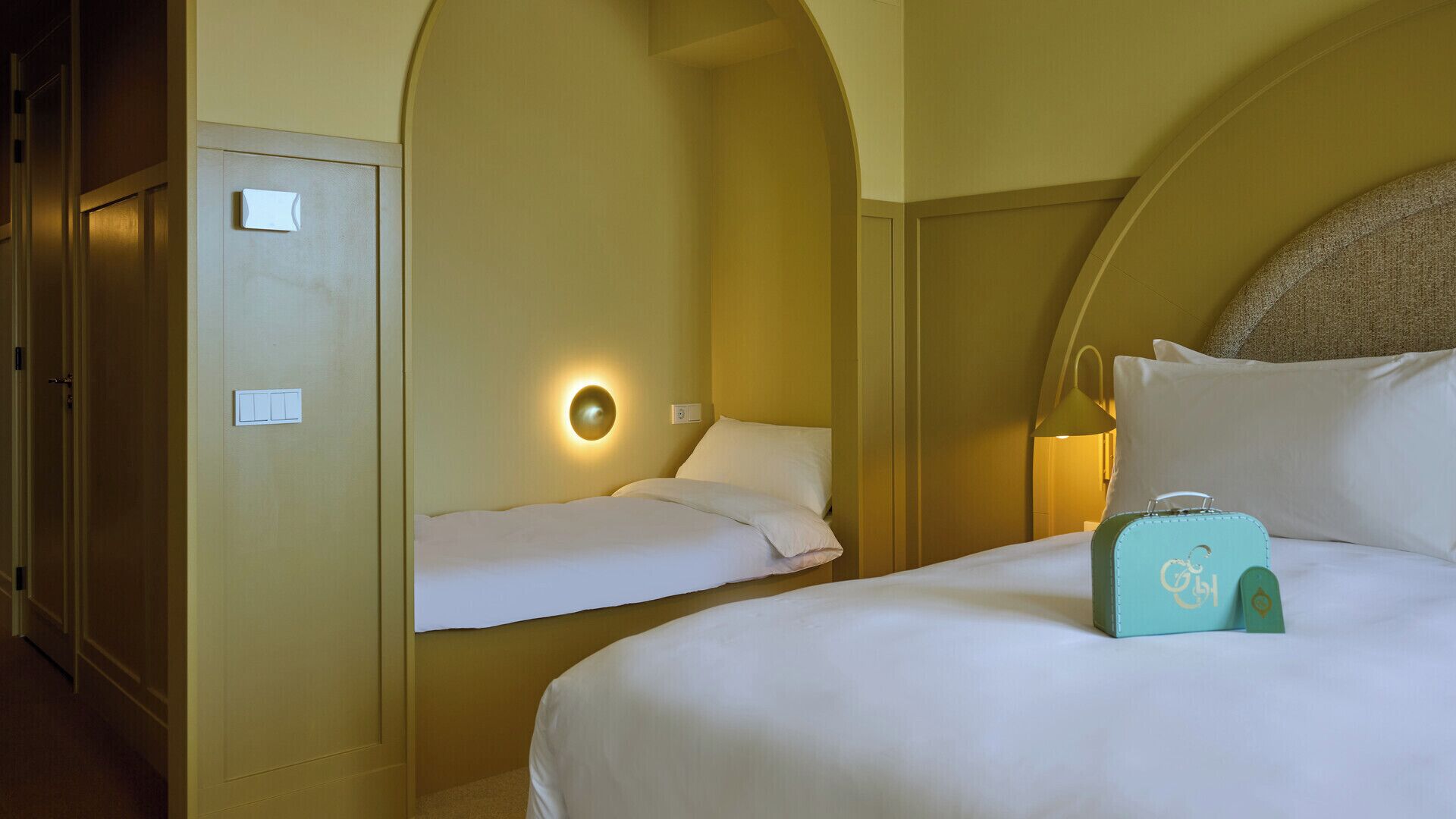 A hotel room with a bed, a bedside table, a lamp, and a suitcase.