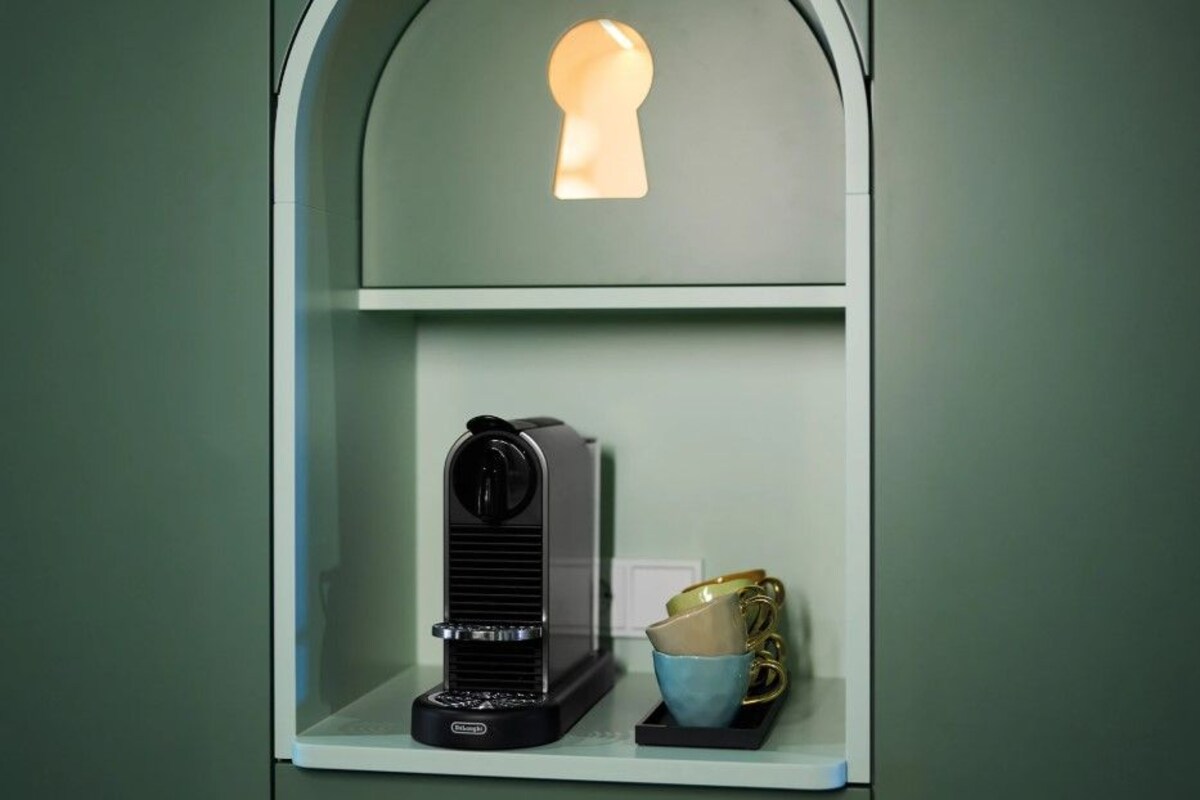 A coffee machine on a shelf with a keyhole above it and a cup holder below.